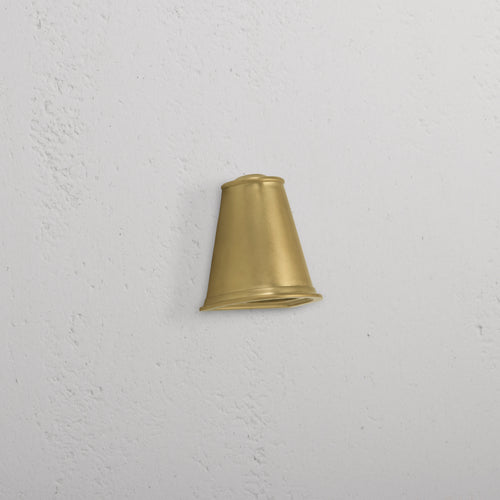 Southwark Mast Light – Antique Brass small wall light with a cone-shaped shade mounted on a white textured wall.