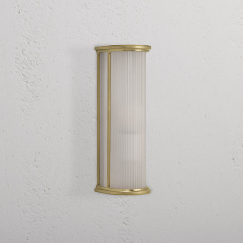 Medium wall light featuring fluted frosted glass and antique brass frame, mounted on a white textured wall.